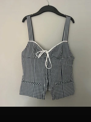 Rutig korsettopp zara - Supersöt korsettopp i svartvitt rutigt mönster med breda axelband och knyt framtill. Toppen har en figurnära passform och vita detaljer längs kanterna. Perfekt för dig som vill ha en trendig och somrig look.❤️