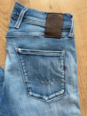 Ljusblå slim  jeans från Replay - Säljer ett par ljusblå skinny jeans från Replay med klassisk femficksmodell och snygga slitningar. Jeansen har en brun läderpatch med Replay-logga bak i midjan och dekorativa sömmar på bakfickan. Perfekta till en avslappnad stil!