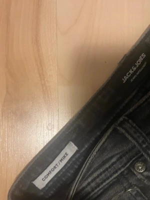 Svarta comfort jeans från Jack & Jones - Säljer ett par svarta comfort fit jeans från Jack & Jones, modell MIKE. Perfekta för dig som gillar en avslappnad och bekväm stil. Materialet är mjukt. Och har ett hål i sig.