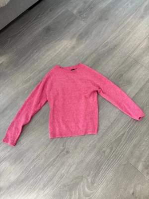 Rosa stickad tröja från Vero Moda - Snygg rosa stickad tröja från Vero Moda med rund halsringning och ribbade muddar vid ärmslut och nederkant. Perfekt för dig som vill ha en enkel men färgglad tröja till garderoben. Materialet är mjukt och bekvämt.