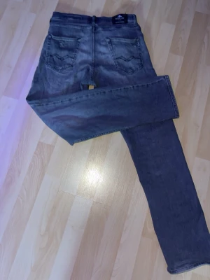 Grå jeans från Replay - Säljer ett par grå jeans från Replay med raka ben och klassiska bakfickor med broderad detalj. Jeansen har normal midja och bälteshällor. Materialet är mjukt denim som ger en avslappnad look. 
