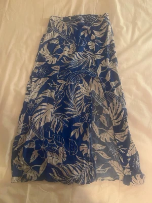 Blåvit långkjol med blommigt mönster - Snygg långkjol i blått och vitt med blommigt mönster. Kjolen har en luftig och flowy passform, perfekt för varma dagar. Elastisk midja för extra komfort och enkel styling. Passar till både sneakers och sandaler.