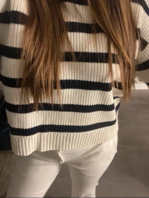 Randig stickad tröja från BikBok - Säljer en krämvit stickad tröja från BikBok med mörkblå horisontella ränder. Tröjan har en avslappnad passform, ribbstickade muddar och är gjord i ett mjukt material. Perfekt för en trendig och bekväm look.