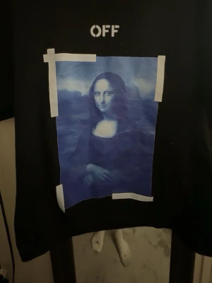 Off-White svart t-shirt Mona Lisa - Svart t-shirt från Off-White med ikoniskt Mona Lisa-tryck i blå toner framtill och vit OFF-text. Knappt använd. 