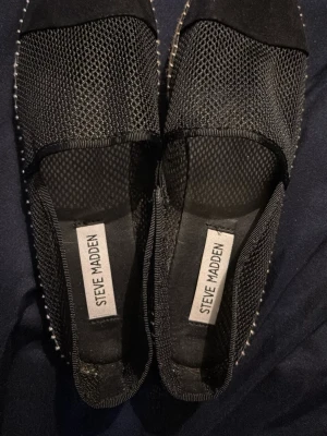 Svarta mesh ballerinaskor Steve Madden - Snygga svarta ballerinaskor från Steve Madden med ovandel i mesh och detaljer i mocka. Skorna har en naturfärgad sula med synliga sömmar och en sportig, luftig känsla. Perfekta för dig som gillar trendiga och bekväma skor. Endast provade inomhus 