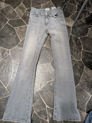 Grå bootcut jeans från only st xs  - Snygga grå jeans från Gina Tricot med bootcut passform och klassisk femficksdesign. Jeansen har en ljusgrå tvätt och subtila slitningar framtill. Tillverkade i mjukt denimtyg som känns bekvämt hela dagen. Midja xs längd 30
