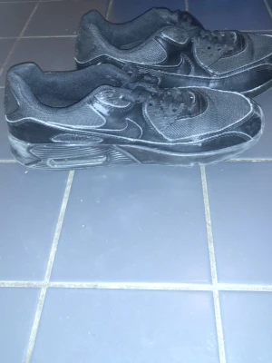 Svarta Nike Air Max sneakers - Säljer ett par helsvarta Nike Air Max sneakers med klassisk siluett. Skorna har ovandel i mesh och syntet, samt den ikoniska Air Max-sulan för extra komfort. Swoosh-logga på sidan och snörning framtill. Perfekta för dig som gillar streetwear och sportig stil.