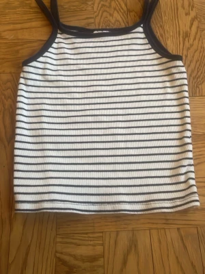 Randig linnetopp från Zara - Säljer en vit och mörkblå ribbad linnetopp från Zara med tunna axelband och horisontella ränder. Toppen har en enkel och clean look och materialet är stretchigt, perfekt till sommaren. Inga fläckar eller sådant (jag hittade inget i alla fall).