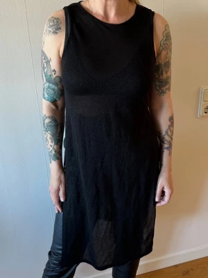 Svart lång ärmlös topp - Snygg svart lång ärmlös topp i transparent material med lätt glittrig finish. Perfekt att styla över linne eller bh för en cool look. Rund halsringning och rak passform som ger en avslappnad vibe.