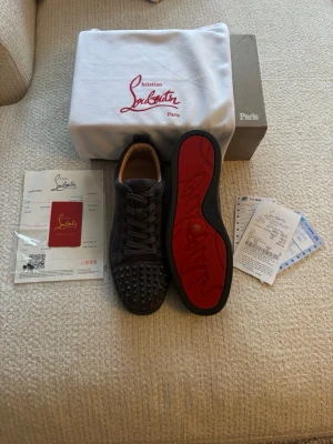 Christian Louboutin - Snygga svarta sneakers från Christian Louboutin i mocka med ikoniska röda sulor och svarta nitar på tån. Skorna har klassisk snörning och låg profil. //har 3 extra spikar med om några av de ramlar..
