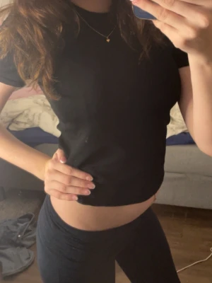 Svart croppad t-shirt från Zara - En enkel svart croppad t-shirt med korta ärmar och rund hals. Perfekt basplagg som är lätt att matcha med olika outfits. T-shirten har en tight passform 