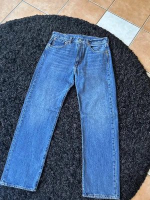 Blå raka jeans från Levi's - Klassiska blå jeans från Levi's med rak passform och fem fickor. Jeansen har en tidlös look med normalhög midja och är tillverkade i slitstark denim. Perfekta för en avslappnad och stilren outfit.