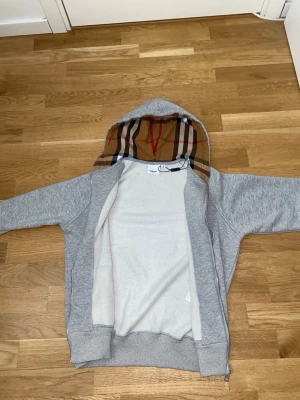 Burberry hoodie - Den är XS men passar S. Snygg grå zip-hoodie från Burberry med klassiskt rutmönster i huvan. Hoodien har dragsko, fickor framtill och ribbade muddar. Perfekt för en chill och stilren look. Materialet är mjukt och bekvämt, passar till många outfits