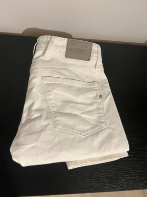 Vita slim fit jeans från replay - Säljer ett par vita slim fit jeans från replay med klassisk femficksdesign och läderpatch bak i midjan. Jeansen har raka ben och är tillverkade i ett mjukt bomullsmaterial. Perfekta för en clean och fräsch look.