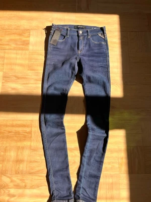 Mörkblå skinny jeans från Replay - Snygga mörkblå skinny jeans från Replay med klassisk femficksdesign och ljusa kontrastsömmar. Jeansen har en smal passform och är tillverkade i stretchigt denim för extra komfort. Perfekta för dig som gillar en stilren och modern look.