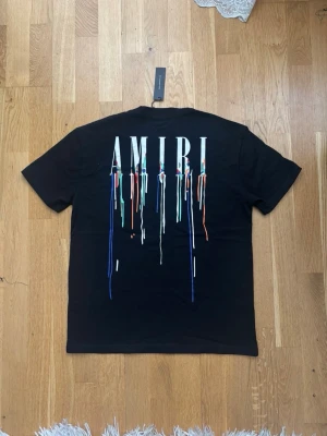 Svart AMIRI t-shirt  - Svart t-shirt från AMIRI med stort vitt logotryck på ryggen och färgglada droppdetaljer. Storlek EU M säljer då den var för stor på mig (fick i present)