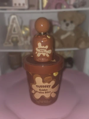 Tubbees Golden Praline Bliss parfym - Tubbees Golden Praline Bliss är en parfym med söt och lyxig känsla. Flaskan är brun med krämfärgade detaljer och har en rund kork. Förpackningen är matchande brun med pralininspirerat mönster. Perfekt för dig som gillar gourmanddofter.