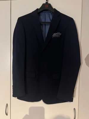 Mörkblå kostym med kavaj och byxor - En mörklblå kostym från dressman. Använd en kväll. Perfekt nu till sommarens baler, eller andra evenemang. Kavajens storlek är 46 slim fit och byxorna 30-32