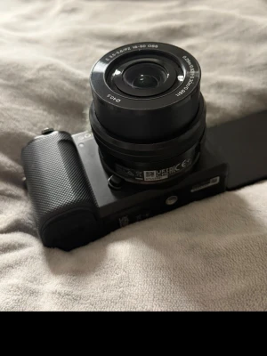 Sony digitalkamera med 16-50mm objektiv - Snygg svart digitalkamera från Sony med ett 16-50mm zoomobjektiv. Kameran har en vridbar skärm och en kompakt design med greppvänligt handtag. Perfekt för vloggning eller foto på språng. Utrustad med mikrofon med vindskydd.