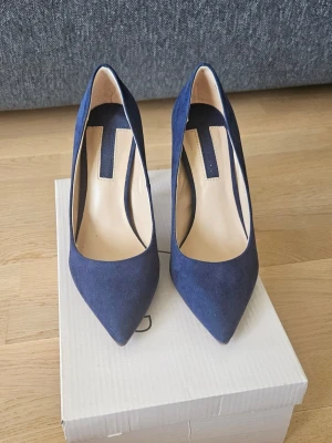 Mörkblåa pumps med spetsig tå - Snygga mörkblå pumps med spetsig tå och höga stilettklackar. Skorna har en klassisk design och är klädda i mockaliknande material. Perfekta för att lyfta din outfit med en elegant touch. Klackhöjd 10 cm. Använd endast 1 gång.