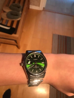 Grön klocka med metallarmband - Snygg klocka från Quartz med en grön skimrande urtavla och tydliga vita markeringar. Klockan har ett klassiskt silverfärgat metallarmband och datumvisning. Perfekt accessoar för dig som vill sticka ut med stilren design.