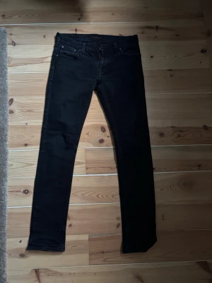 Svarta skinny jeans från nudie - Säljer ett par svarta skinny jeans från Lee med klassisk femficksdesign och smal passform. Jeansen har svarta sömmar och nudie logga på bakfickan. Materialet är stretchigt för extra komfort och sitter tight hela vägen ner.