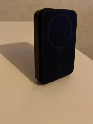 Belkin MagSafe powerbank svart - En svart magnetisk powerbank med stativ. Snygg och smidig svart MagSafe powerbank från Belkin. Rektangulär form med rundad kant, magnetisk yta för enkel fastsättning på baksidan av mobilen och ett utfällbart ställ på baksidan. Perfekt för trådlös laddning när du är på språng.