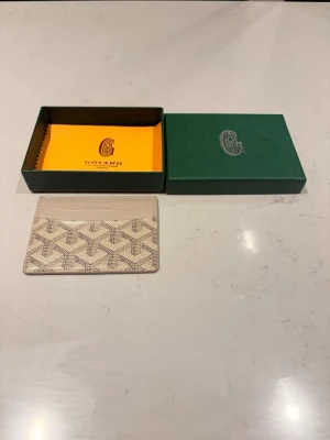 Beige kortfodral - Snyggt och stilrent kortfodral i beige och vitt med det klassiska mönstret. Tillverkat i canvas och läder, perfekt för kort och ID. Kommer med original ask och putsduk.