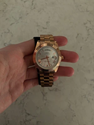 Rosé guldfärgad klocka från Nibosi - Snygg rosé guldfärgad klocka från Nibosi med metallarmband och vit urtavla. Klockan har dag- och datumvisning samt tydliga markeringar och visare i guld. Aldrig använt och inte fixad i storlek men jag skickar med ett sett för att fixa storleken på klockan vid köp. Pris går att diskutera