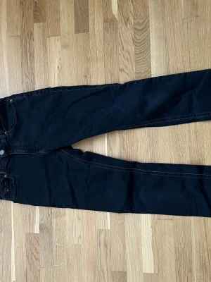Svarta skinny jeans Tommy Hilfiger - Säljer ett par svarta skinny jeans från Tommy Hilfiger. Klassisk femficksmodell med knapp och dragkedja. Snygga röda och vita detaljer på insidan av linningen. Perfekta för dig som gillar stilrena och tidlösa jeans. Använda väldigt fåtal gånger och det syns inte på dem alls
