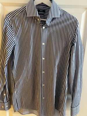 Randig skjorta från BOSS i bomull - Snygg skjorta från BOSS med vertikala svarta och vita ränder. Klassisk krage, långärmad och knäppning framtill med vita knappar. 