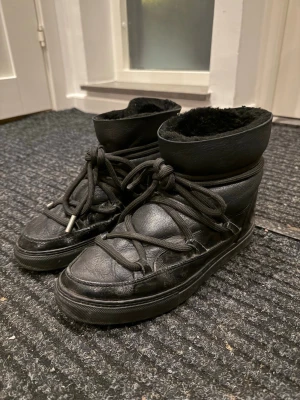 Svarta vinterskor från Inuikii - Säljer ett par svarta vinterskor från Inuikii med högt skaft, grova snören och mjuk fuskpäls på insidan. Skorna är i läder. Perfekta för kalla dagar när du vill vara både varm och snygg.