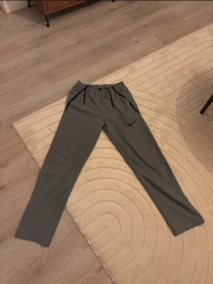 Grå Nike mjukisbyxor med logga - Säljer ett par grå mjukisbyxor från Nike med svart logga på benet. Byxorna har resår i midjan och svarta detaljer vid fickorna. Perfekta för chill dagar eller träning. Materialet känns lätt och smidigt.