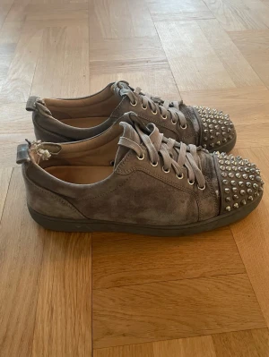 Grå Christian Louboutin - Gråa skor med nitar av märket Christian Louboutin, helt OK skick men har defekt (se bild 4 ), därefter billigare pris. Storlek 42-43, hör av dig vid funderingar! * Fraktas samma dag som köp (gäller vid köp innan kl 18.00).