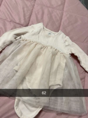 Ljus babyklänning med tyllkjol - Supersöt babyklänning i ljus färg med långärmad ribbad överdel och mjuk tyllkjol. Klänningen har tryckknappar i grenen för enkel påklädning och är perfekt för speciella tillfällen.