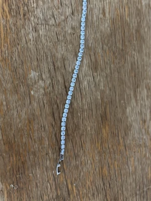 Silverfärgat tennisarmband med stenar - Snyggt silverfärgat tennisarmband med gnistrande klara stenar i rad. Armbandet har en klassisk, elegant design och stängs med ett smidigt spänne. Perfekt för dig som gillar stilrena accessoarer med lite extra bling.