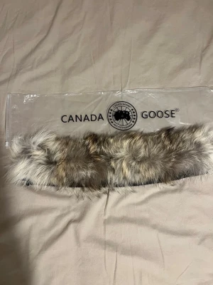Pälskrage från Canada Goose - Säljer en fluffig pälskrage från Canada Goose i naturfärgad äkta päls. Kragen har dragkedja på baksidan och passar perfekt till jackor med avtagbar huva. Kommer i originalpåse från Canada Goose.