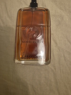 Gucci Guilty Absolute Pour Homme EdP - Gucci Guilty Absolute Pour Homme Eau de Parfum i en stilren, rektangulär glasflaska med bärnstensfärgad vätska. Flaskan har präglad Gucci-logga och svart spraymunstycke. En maskulin doft som sticker ut och passar dig som gillar exklusiva parfymer. 70ml finns kvar