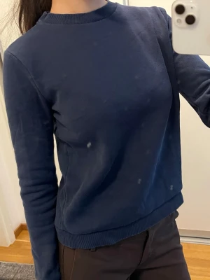 Mörkblå sweatshirt från Nelly - En stilren mörkblå sweatshirt med rund hals och långa ärmar. Tröjan har ribbade muddar vid ärmslut och nederkant. Perfekt för en avslappnad och enkel look. Materialet känns mjukt och bekvämt mot huden.