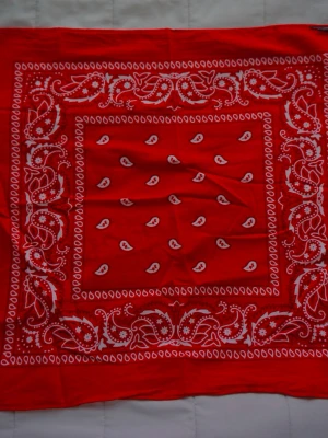 Röd bandanasjal med paisleymönster - Snygg röd bandanasjal med klassiskt vitt paisleymönster. Fyrkantig form och tunn, mjuk bomullskänsla som gör den enkel att styla runt halsen, i håret eller på väskan. Perfekt accessoar för att addera färg och edge till din outfit.