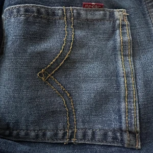 Levi's 512 Slim Taper jeans blå - Säljer ett par klassiska jeans från levis med modellen levis 512 Slim Taper jeans i blå denim med snygga kontrastsömmar och ikonisk bakficka. Jeansen har smal passform och avsmalnande ben, perfekt för en modern look. Typisk Levi's-lapp syns vid bakfickan. Jeansen är i ett bra skick och perfekta inför våren!