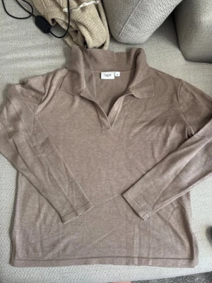 Beige långärmad tröja från Saint - Säljer en stilren beige långärmad tröja från Saint med krage och v-ringad öppning. Tröjan har en mjuk och tunn stickning som passar perfekt till lager på lager och ger en avslappnad men snygg look.