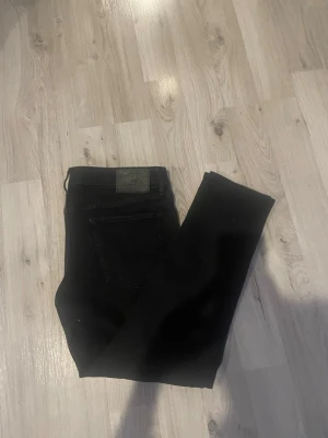 Svarta jeans från jack Jones  - Snygga svarta jeans från Jack Jones med klassisk femficksdesign och diskret logga på bakfickan. Jeansen har en smal passform och är tillverkade i stretchigt denimtyg för extra komfort.