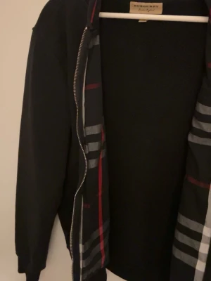 Svart hoodie från Burberry - Snygg svart hoodie från Burberry med dragkedja. Tröjan är i perfekt skick, inga skador. Noppor eller fläckar finns på tröjan. Använd runt 7 gånger totalt.