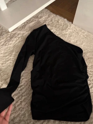 Svart oneshoulder topp - Snygg svart oneshoulder topp med lång ärm. Toppen har en stilren och enkel design som passar perfekt till olika outfits. Materialet känns mjukt och följsamt mot kroppen.