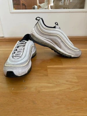 Nike Air Max 97 vita sneakers Storlek 39 - Nike Air Max 97 sneakers i vitt och grått med ikoniska vågformade paneler och synlig Air Max-sula. Storlek 39, 25 cm. Kan skickas eller hämtas upp i Farsta, Stockholm.
