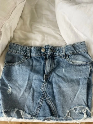 Blå jeanskjol - Säljer en blå jeanskjol i kort modell med rå, fransig kant nertill och fina fickor från Gina 