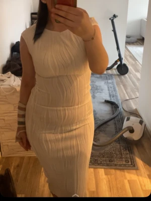 Vit ribbad långklänning - Säljer en elegant vit långklänning med ribbad struktur och ärmlös design. Klänningen har en kroppsnära passform och rund halsringning, perfekt för dig som gillar stilrena och moderna plagg.