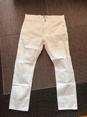 Vita raka jeans från 157 - Snygga vita jeans från 157 med rak passform och klassisk femficksdesign. Jeansen har knappgylf och är tillverkade i ett kraftigare bomullstyg som ger en clean och fräsch look. Perfekta för dig som vill sticka ut med stilrena vita jeans. 36/32