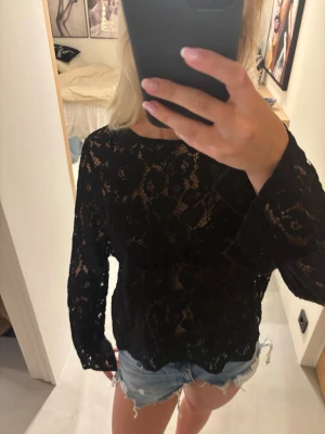 Svart spetsblus med lång ärm - Säljer en svart blus i genombruten spets med lång ärm och rund hals. Blusen har ett knyte i ryggen och passar perfekt till fest🌸